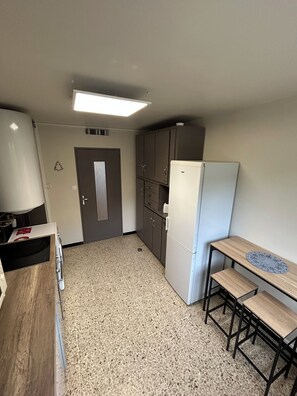 A compact kitchen with a refrigerator, cabinets, a microwave, and a small wooden table with stools.