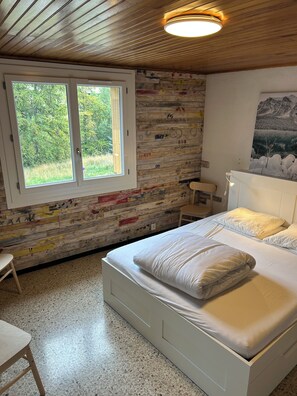 A bedroom with a bed, a window, a wall with a wooden plank design, and a ceiling light.