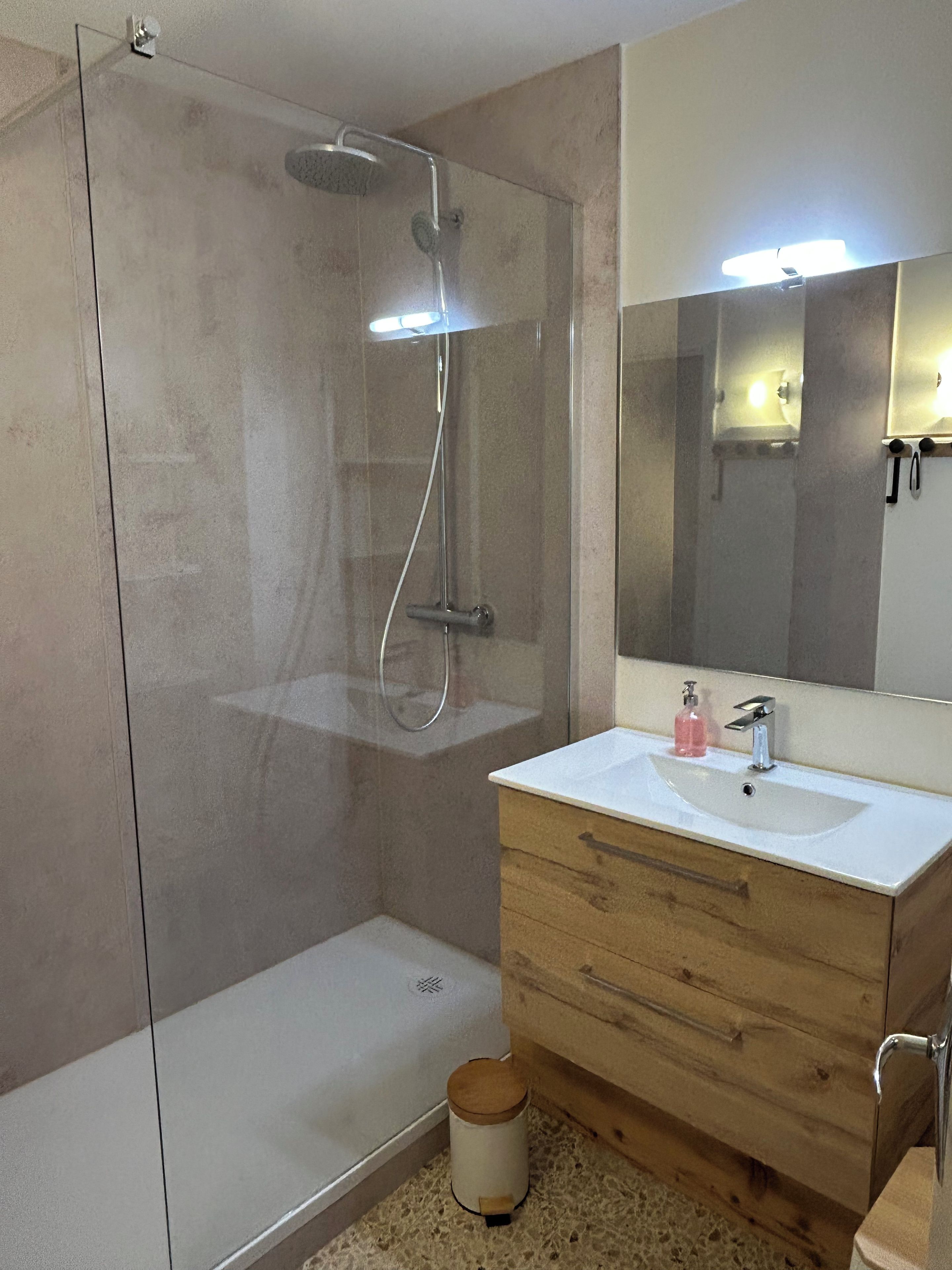 A bathroom with a glass-enclosed shower, a wooden vanity with a sink, and a mirror above the vanity.
