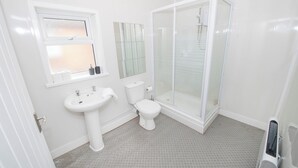 Et moderne badeværelse med en glasafskærmet brusekabine, et pedestalvask og et toilet.