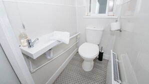 Et lille, moderne badeværelse med hvid vask, toilet og brusebad.