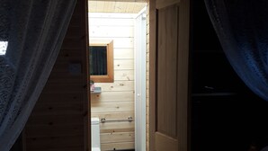 Una habitación tipo cabaña de madera con una cama, un ventanal pequeño y una puerta que da a un baño.