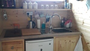 Cocina compacta con paredes de madera, un lavamanos empotrado, un refrigerador pequeño y una ventana sobre el lavamanos.