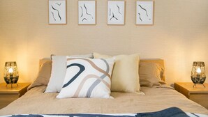 Een slaapkamer met een bed, twee nachtkastjes en vier abstracte kunstwerken aan de muur.