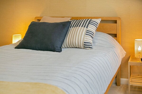 A neatly made bed with striped bedding and two pillows, a wooden headboard, and a bedside table with a lamp.