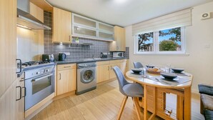 Een moderne keuken met een ingebouwde oven, magnetron en wasmachine. Er is een eethoek met een tafel en stoelen.