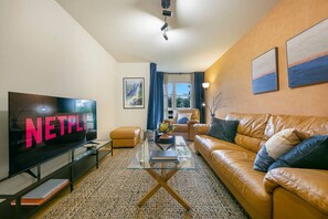 Un salon moderne avec un canapé en cuir, une table basse en verre, un téléviseur à écran plat et une grande fenêtre avec des rideaux.