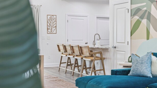 Ein modernes Wohnzimmer mit einem blaugrünen Sofa, einem Holzespeisetisch mit vier Stühlen und einer Küchenzeile mit weißen Schränken und einer Spüle.