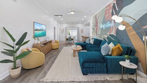 Ein modernes Wohnzimmer mit einem türkisfarbenen Sofa, einem gelben Sessel und einem großen abstrakten Wandbild.