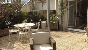 An outdoor patio area with wicker furniture, a table, and chairs. There are potted plants and a metal bucket on the ground. - 2 rooms old lille, superb terrace, parking (Lille)