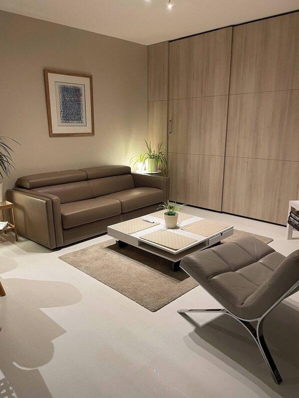 A modern living room with a brown leather sofa, a white coffee table with a plant, and a grey armchair.