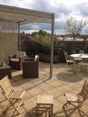 A covered patio area with wicker furniture, a small table, and a white chair.