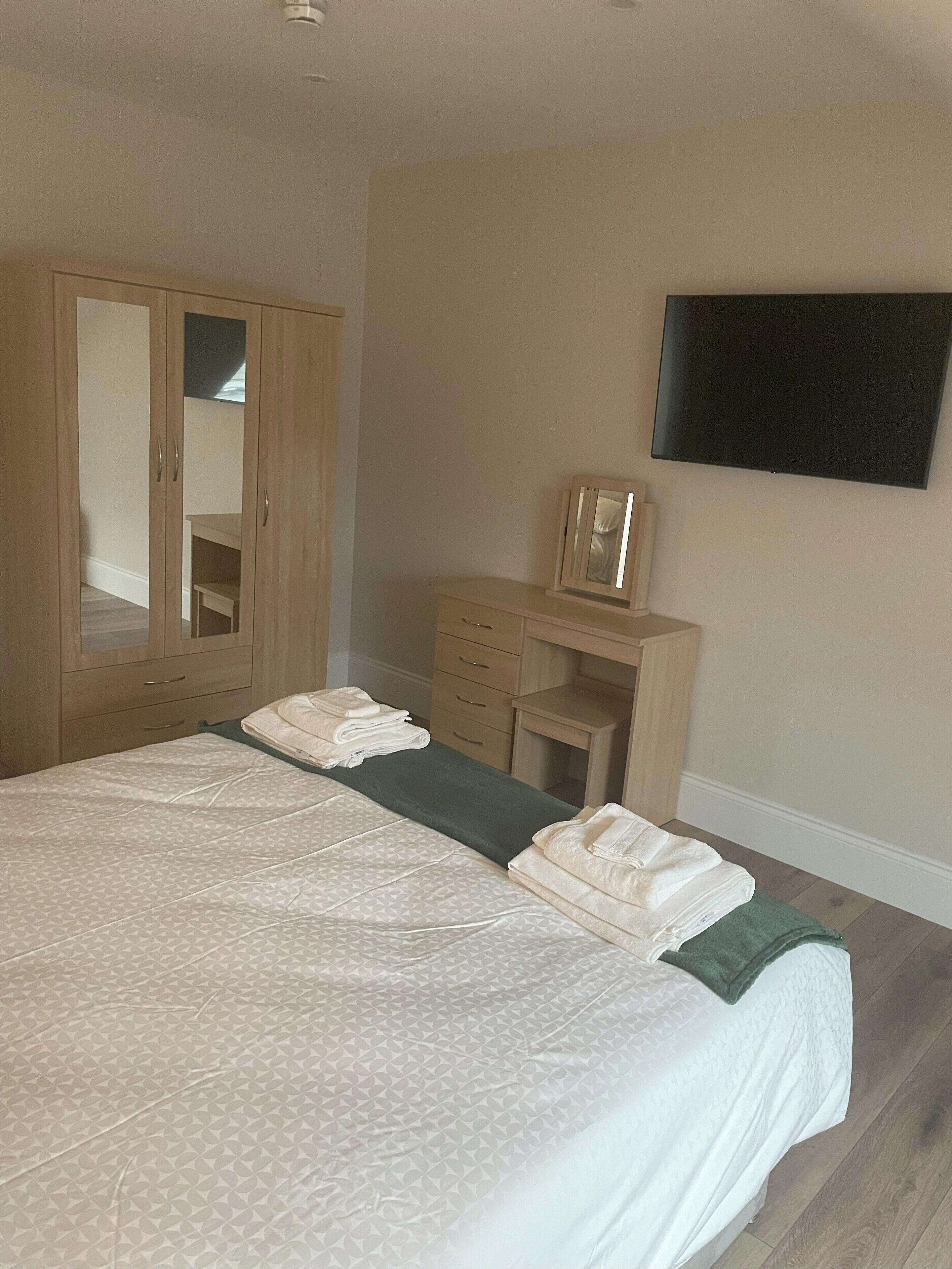 A bedroom with a bed, a wardrobe, a desk, and a flat-screen TV.