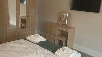 A bedroom with a bed, a wardrobe, a desk, and a flat-screen TV.