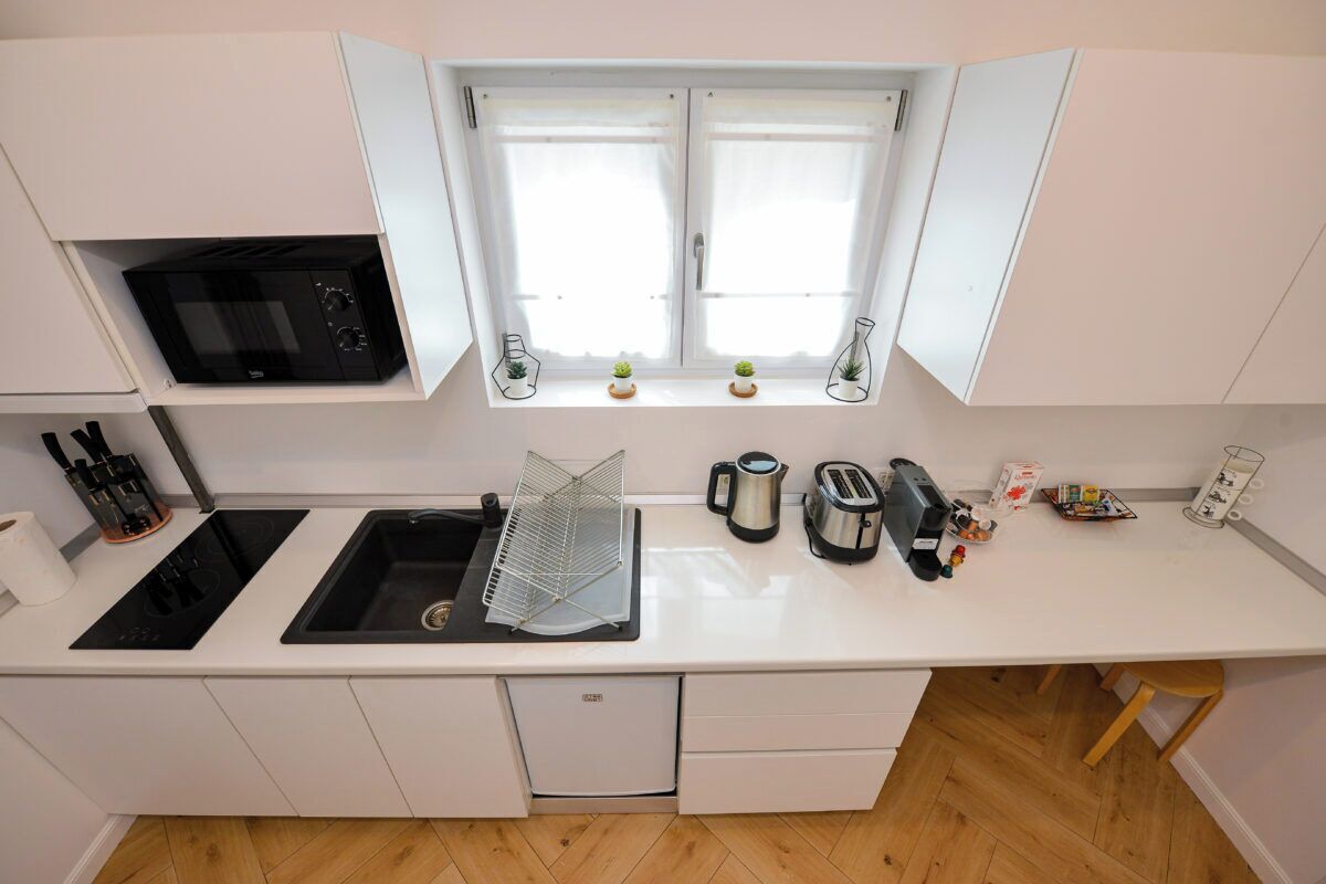 A compact kitchen with a microwave, sink, and a window with two small potted plants.