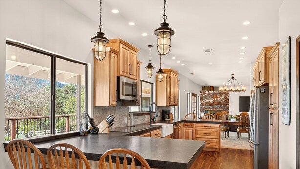 A modern kitchen with wooden cabinets, a large island with bar stools, stainless steel appliances, and pendant lighting. - Amazing Views, Secluded property, 2025 Remodeled, Near Yosemite & Amenities (Oakhurst)