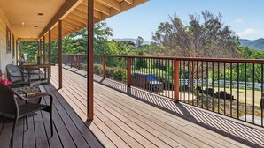 A covered outdoor deck with a table and chairs, overlooking a green landscape and mountains. - Amazing Views, Secluded property, 2025 Remodeled, Near Yosemite & Amenities (Oakhurst)