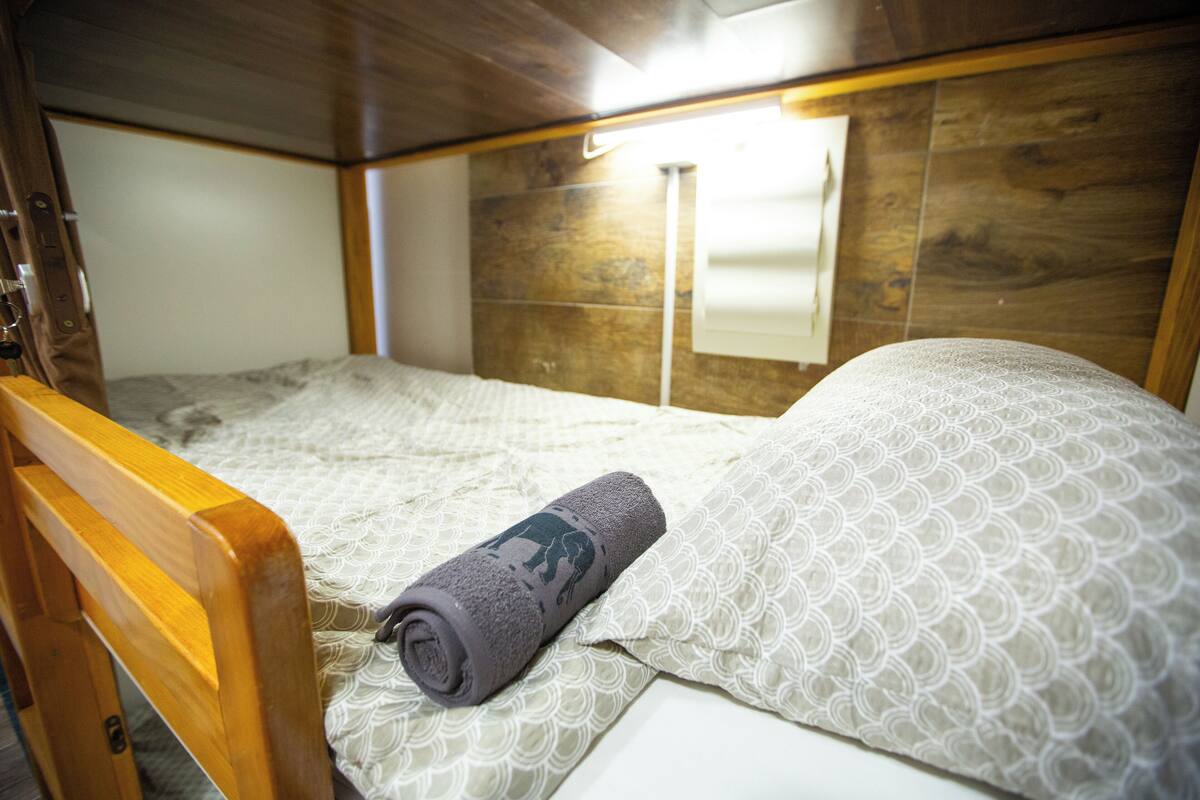 A small, wooden-framed bed with a rolled-up towel and patterned pillows.