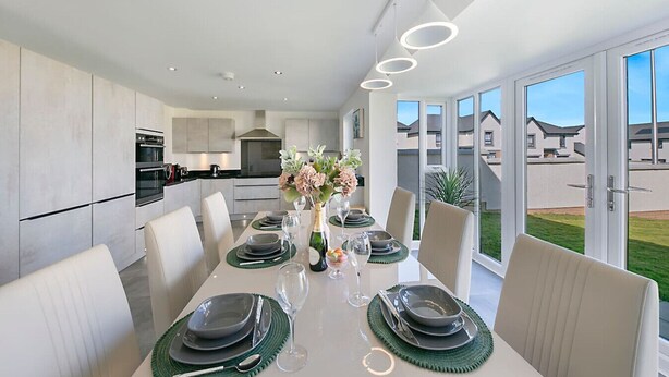 A modern kitchen with built-in appliances and a dining area with a long table set for six. - Fern Place Villa  | Grampian Lettings Ltd (Aberdeen City)