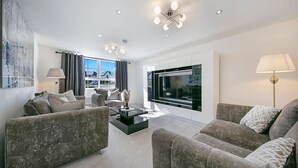 A modern living room with two grey sofas, a coffee table, a TV, and a large window with curtains. - Fern Place Villa  | Grampian Lettings Ltd (Aberdeen City)