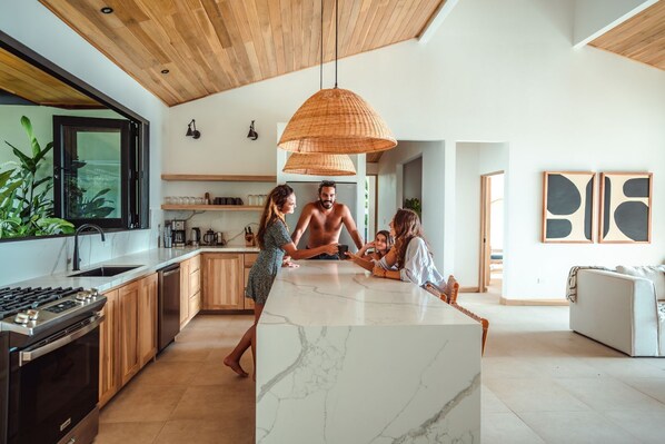 Une cuisine moderne dotée d’un grand îlot central, de meubles en bois et d’un luminaire suspendu.