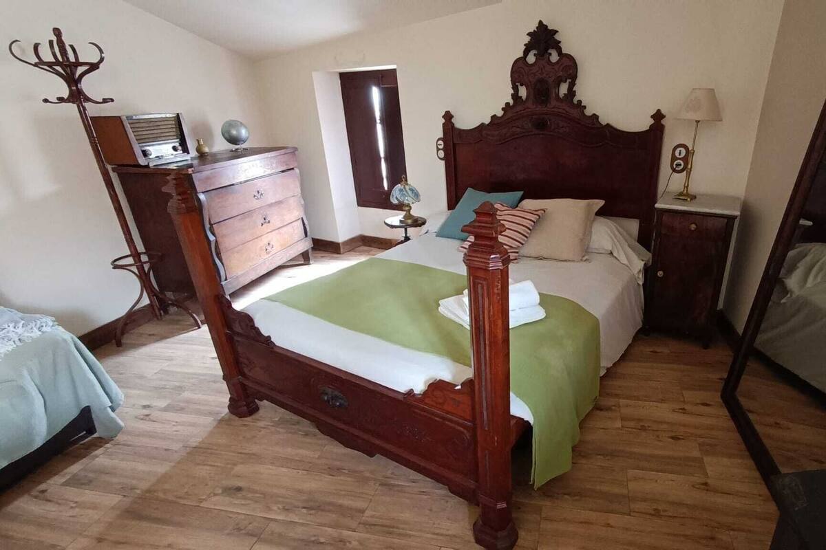 A traditional wooden bed with a green bedspread, a dresser with a globe and radio, and a large mirror.