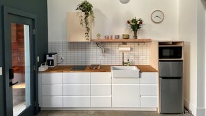 Une cuisine moderne avec des meubles blancs, un plan de travail en bois, un réfrigérateur en acier inoxydable et une plante suspendue.
