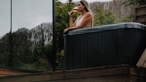 Une personne est assise sur une terrasse en bois, devant une grande baie vitrée, avec vue sur une zone boisée.