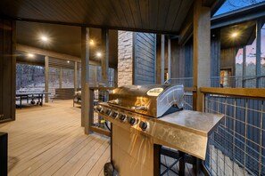 An outdoor barbecue area with a stainless steel grill, wooden deck, and a stone wall. - Sleeps 20 | Secluded, Pond & Loaded Game Room! (Broken Bow)