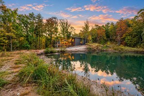 A lakeside cabin with a view of the sunset, surrounded by dense forest.