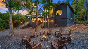 Eine moderne Holzhütte mit Feuerstelle und Adirondack-Stühlen in einer Waldlandschaft.
