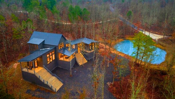 Ein modernes Haus mit mehreren Ebenen, einer großen Terrasse und einem Teich.