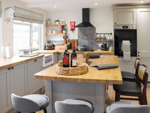 Une cuisine moderne avec des plans de travail en bois, un îlot central doté de tabourets, une cuisinière encastrée et un porte-casseroles suspendu.