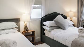 Una cama bien hecha con almohadas y una toalla enrollada, una mesita de noche con una lámpara y una ventana con cortinas.