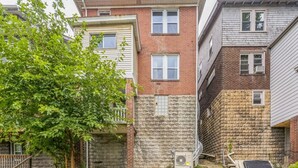 Un immeuble résidentiel à plusieurs étages, avec une façade en briques et en bardage, un mur en pierre et un arbre au premier plan.