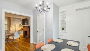 Un coin repas avec une table dressée pour quatre personnes, un lustre et une vue sur un salon doté d’une cheminée.