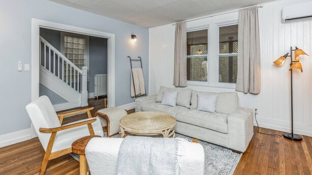 Un salon comprenant un canapé, des fauteuils, une petite table, un escalier et un radiateur.