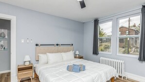 Une chambre à coucher avec un lit, des tables de chevet, un radiateur et une fenêtre avec des rideaux.