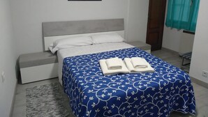 Un dormitorio con cama, mesita de noche, una alfombra pequeña, un cuadro en la pared y ventana con cortinas.