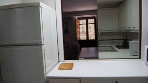 Una cocina con armarios blancos, un refrigerador, un microondas y una tabla de cortar de madera en la encimera.