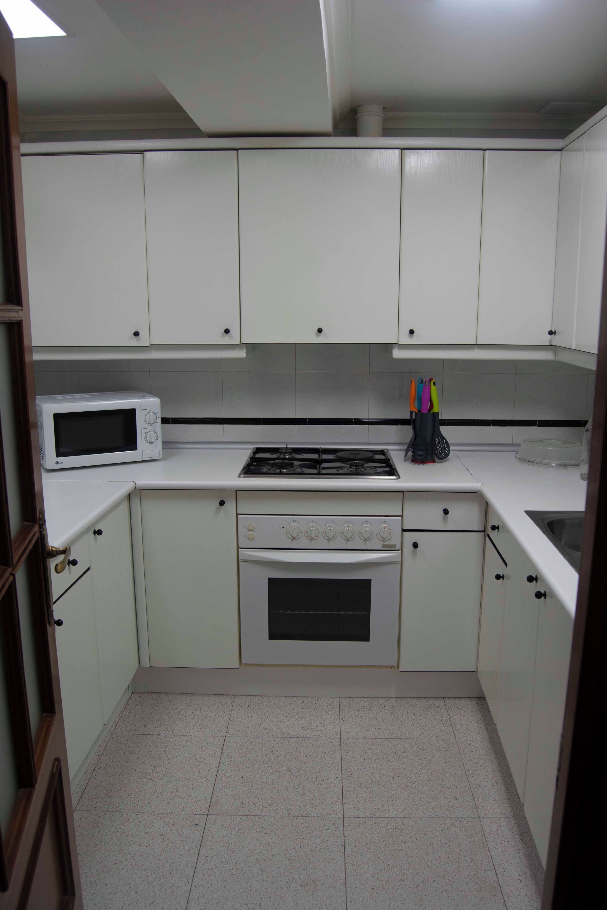 A compact kitchen with white cabinets, a microwave, a stove, and a sink.
