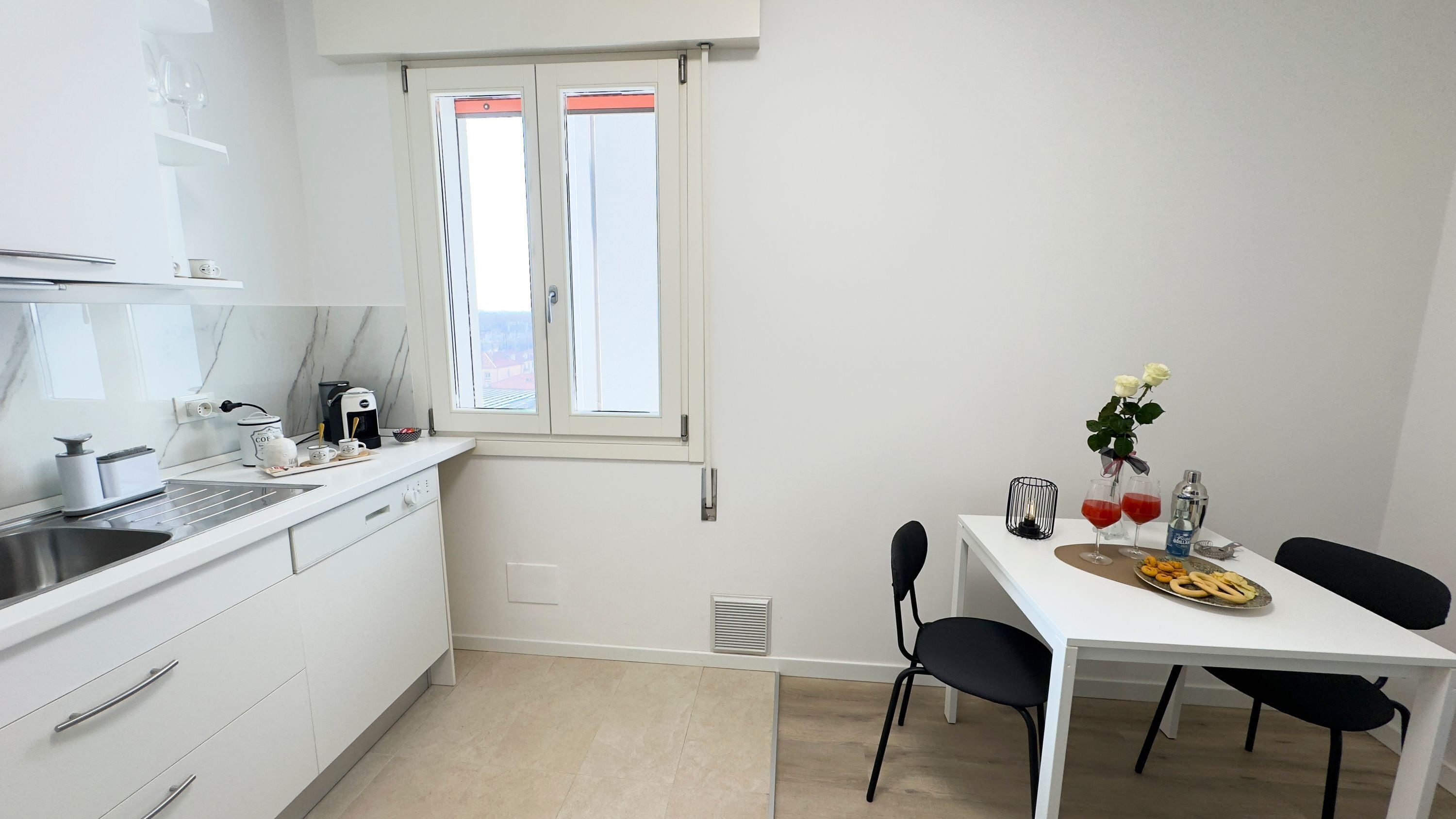 A modern kitchen with white cabinets, a built-in oven, and a window with blinds.
