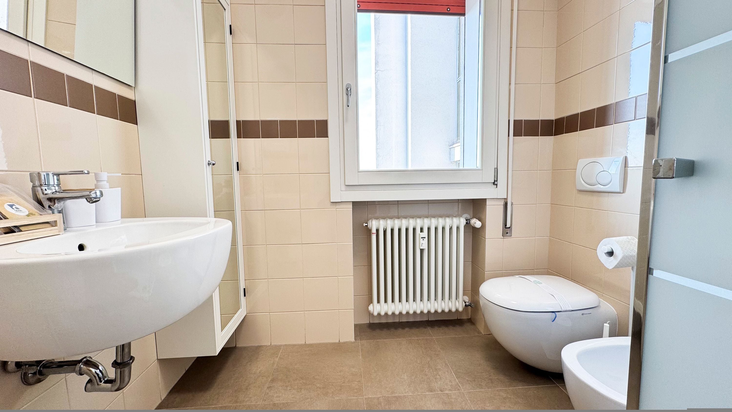 A bathroom with a white sink, a toilet, and a window above the toilet.