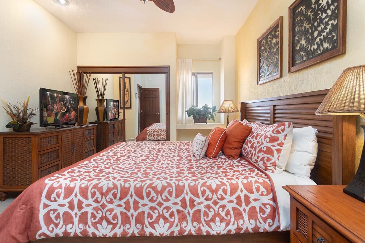 Une chambre à coucher avec un grand lit, une tête de lit en bois et un téléviseur posé sur une commode en bois.