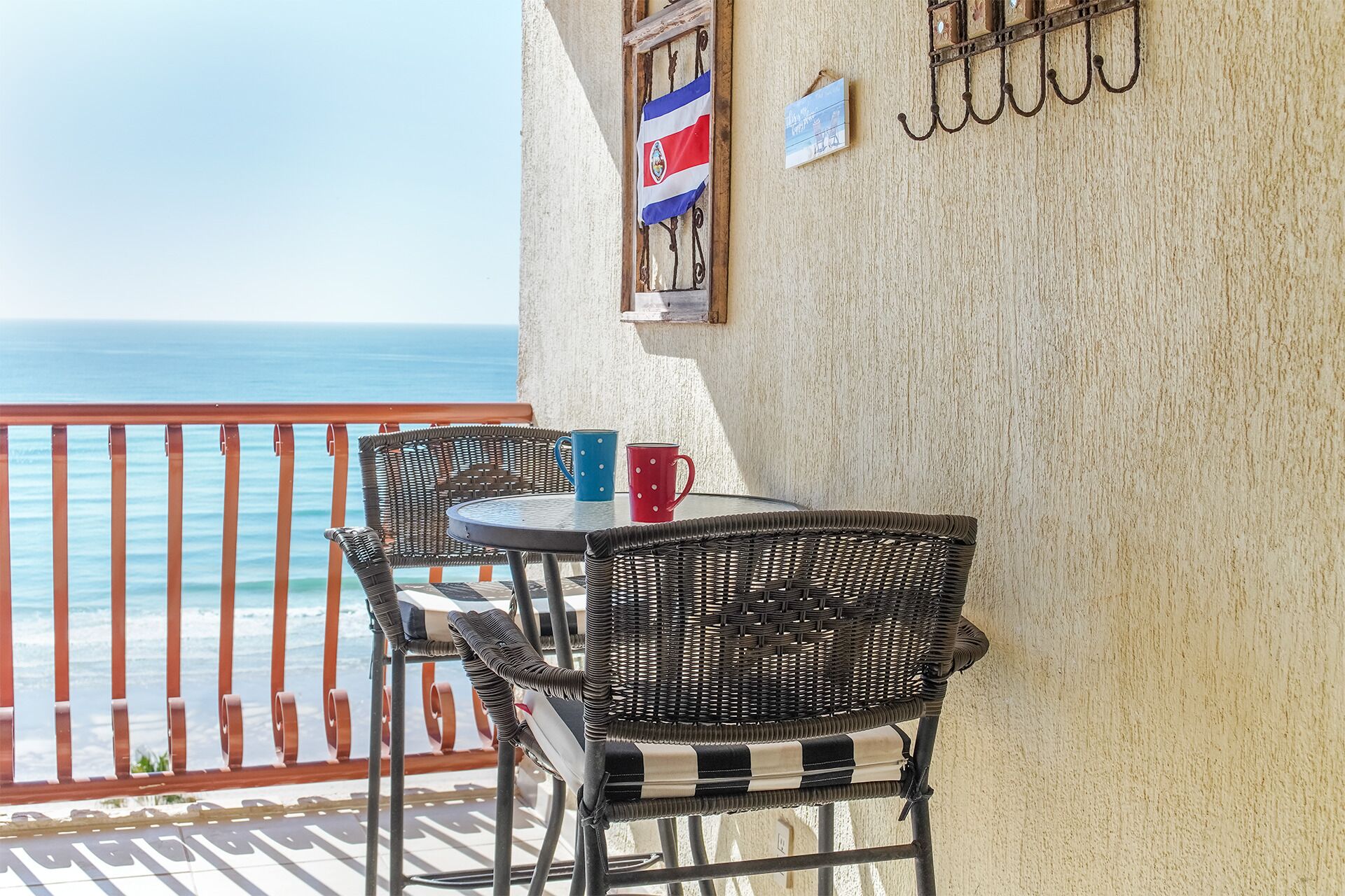 A balcony with wicker chairs and a table, a flag, and a view of the ocean.