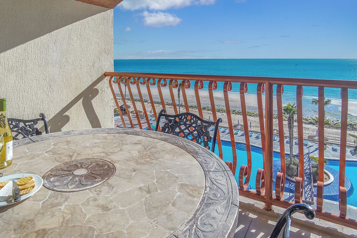 A balcony with a stone table, a bottle of wine, and a plate with crackers and cheese.
