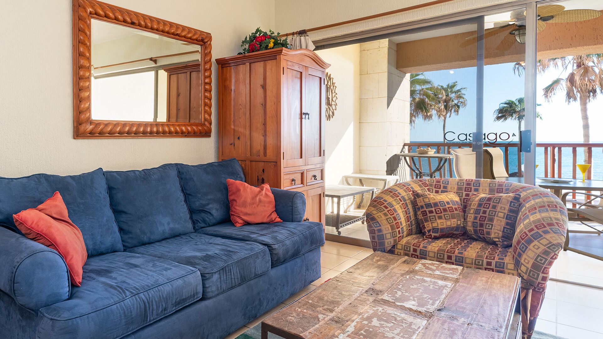 Ein Wohnzimmer mit einem blauen Sofa, einem gemusterten Sessel, einer Holzkabine und einem großen Spiegel.
