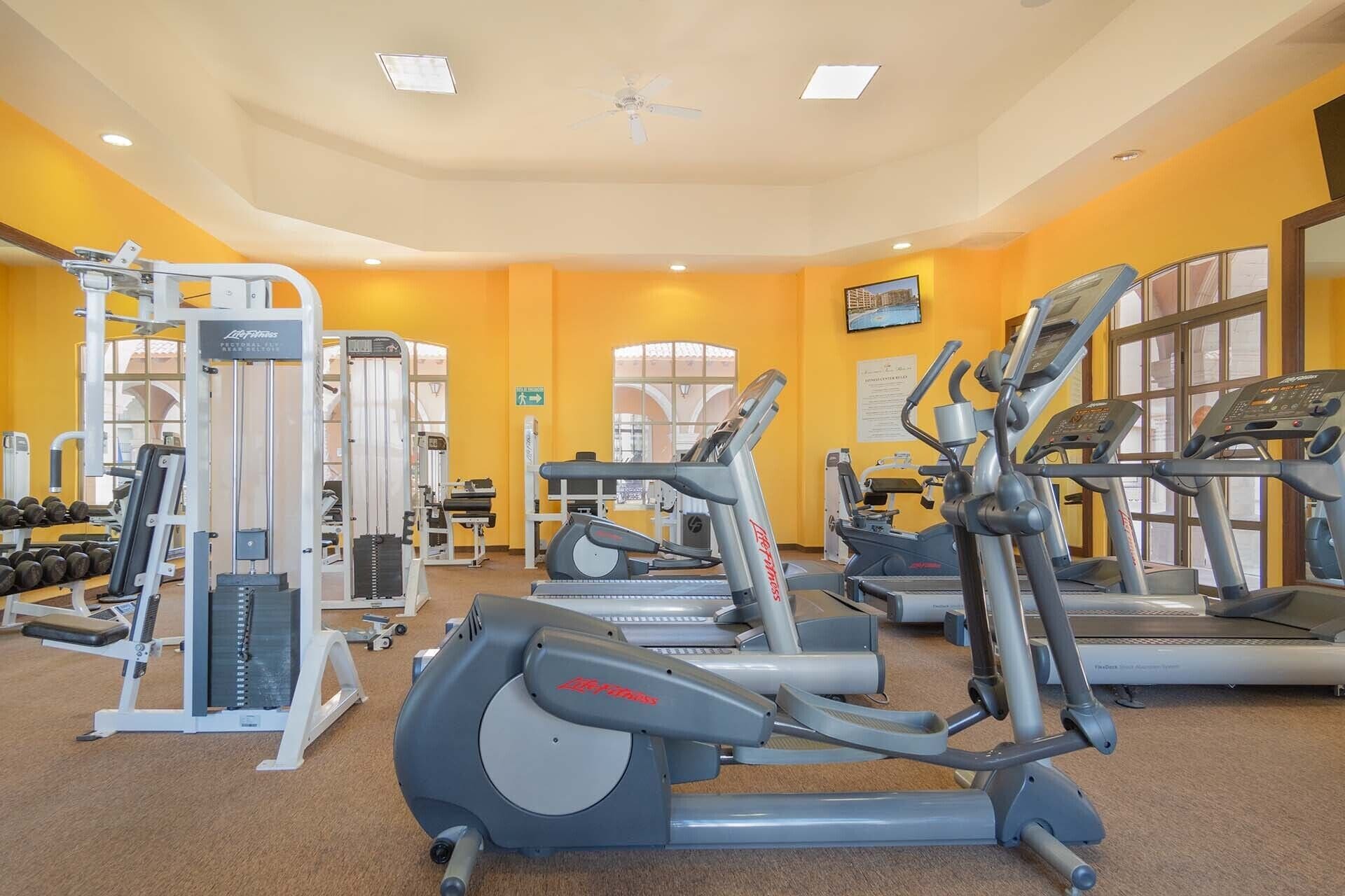 Un gimnasio con cintas de correr, elípticas y equipo de levantamiento de pesas.