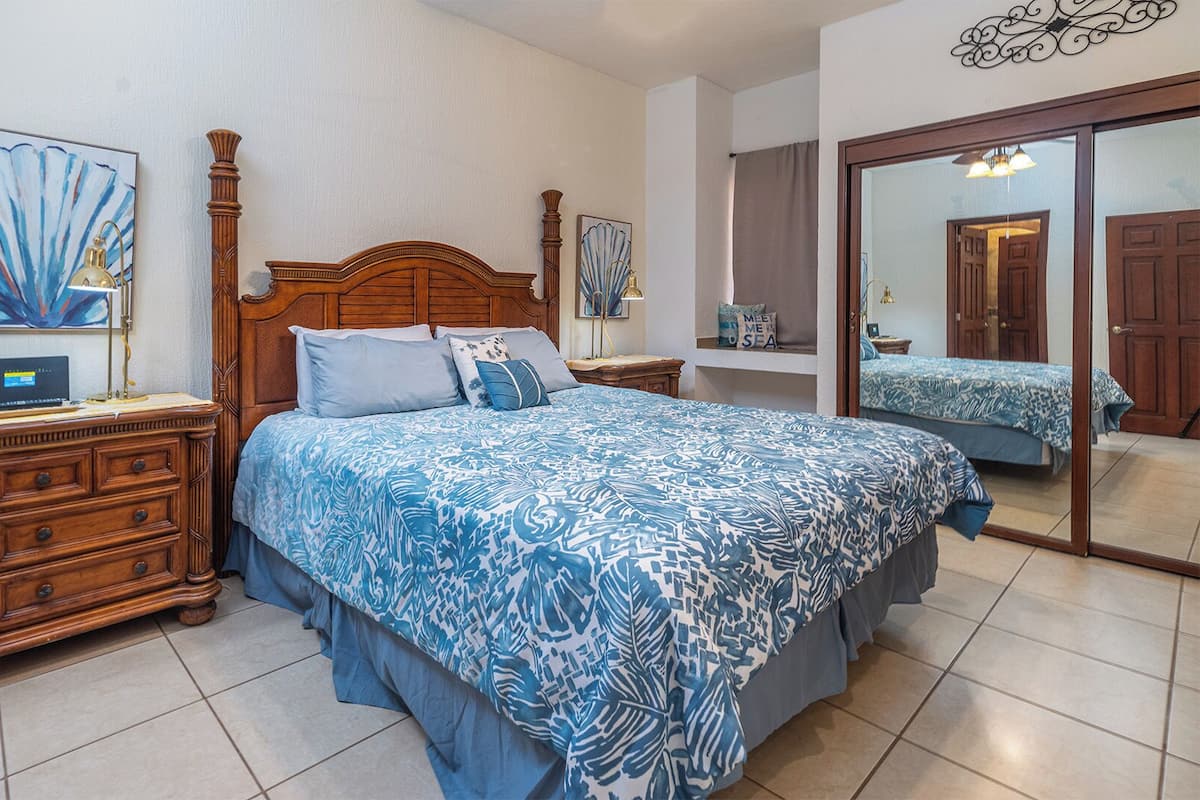 Une chambre à coucher avec un lit en bois, une table de chevet, une commode et un grand miroir.