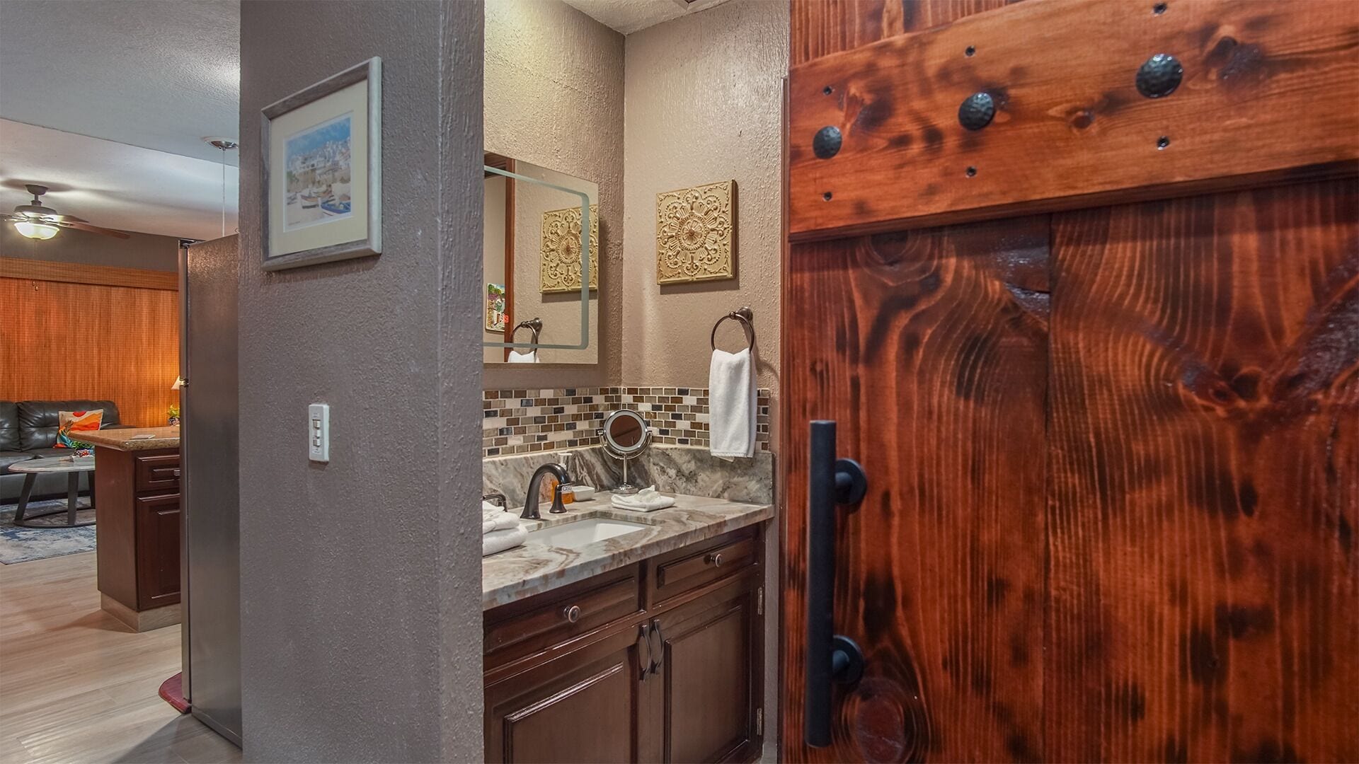 A modern kitchen with a marble countertop, wooden cabinets, and a large wooden door with a metal handle.